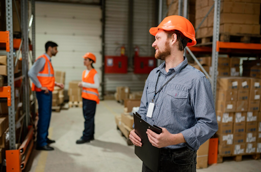 Warehouse manager holding a clipboard with workers in the background